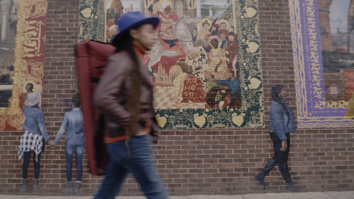 Person walking in front of a mural on a brick wall